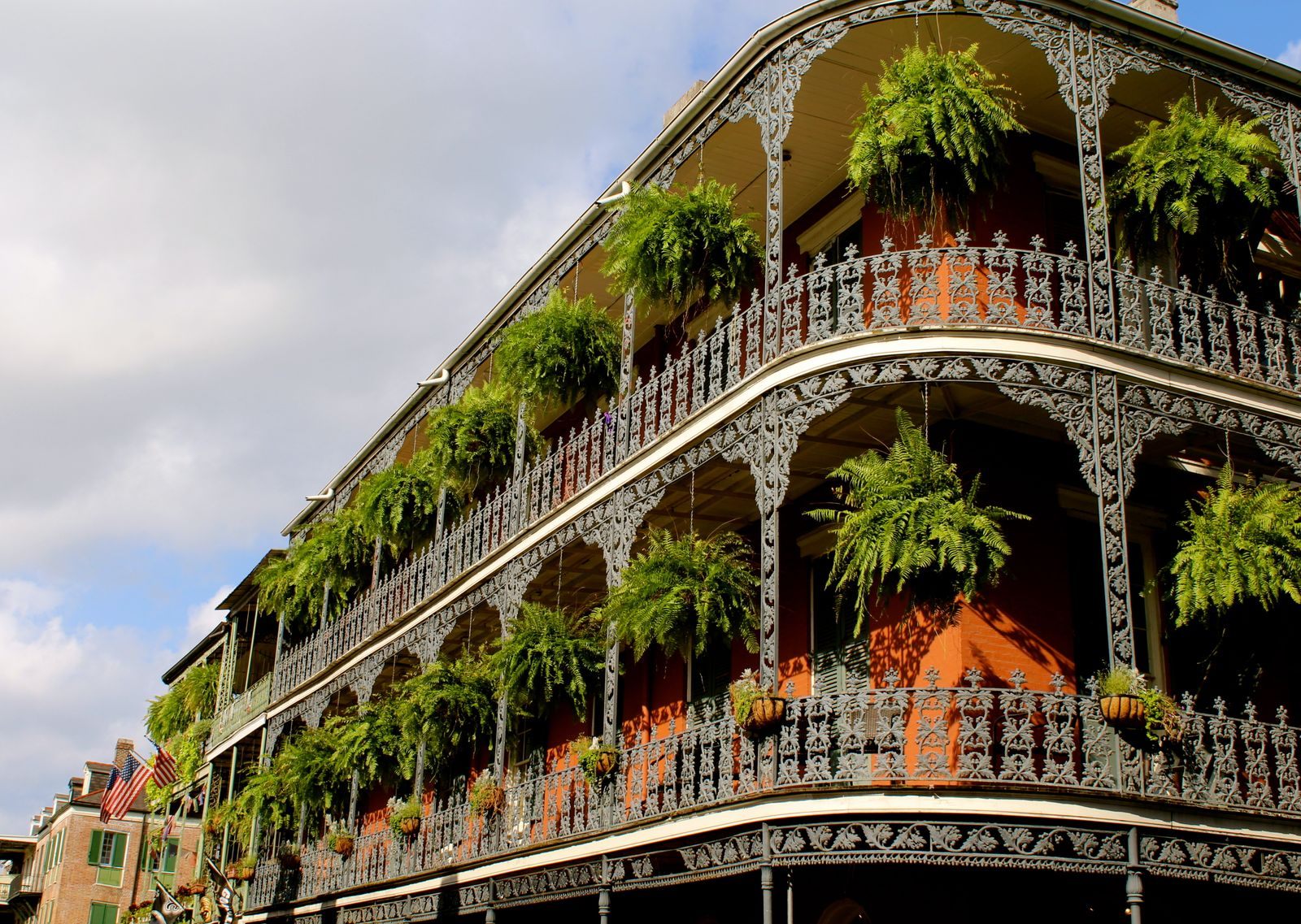 A corner building in New Orleans with two levels of ornate cast-iron balconies hung with ferns