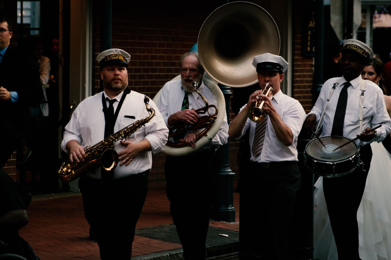 Members of a brass band in white shirts and caps playing saxophone, sousaphone, trumpet and drum
