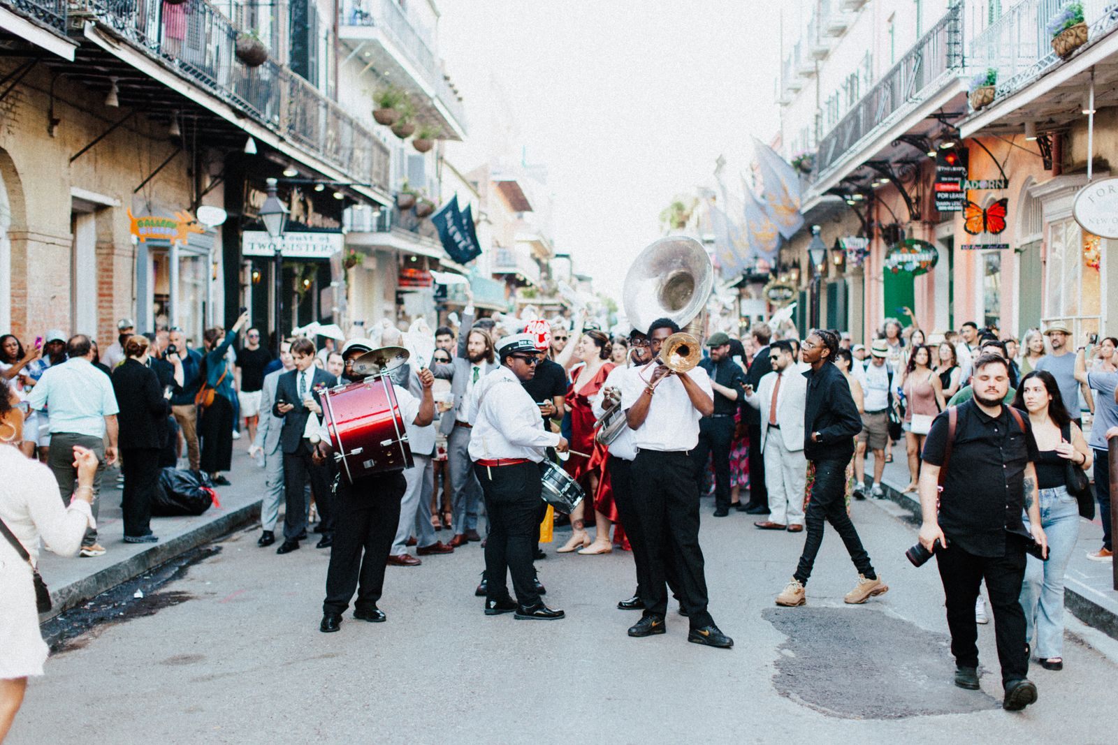 A brass band leading a street parade past a crowd on a New Orleans street lined with balconies