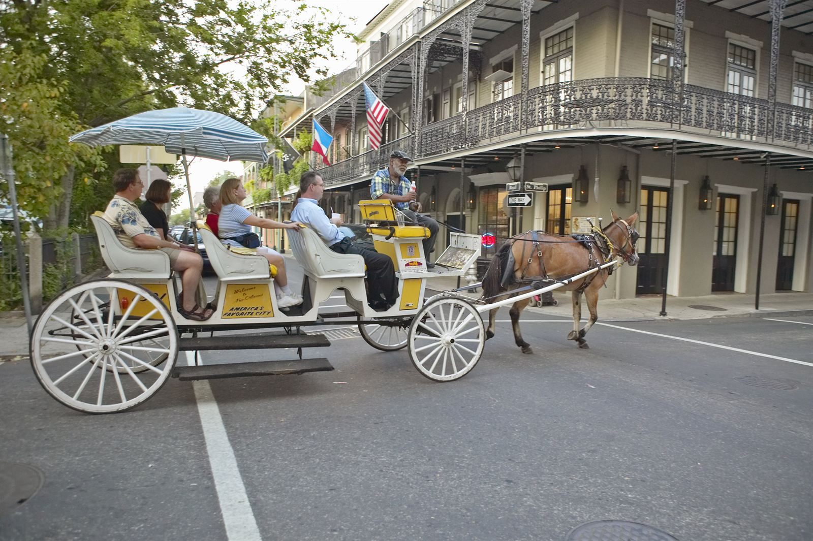 A mule-drawn carriage carrying visitors past a French Quarter building with wraparound cast-iron balconies