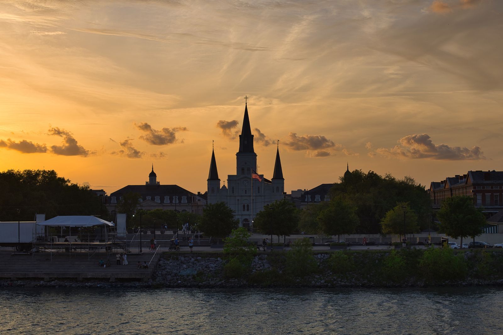 The spires of St. Louis Cathedral silhouetted against an orange sunset, seen across the Mississippi River in New Orleans